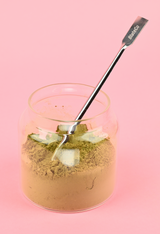 Glass jar with green supplement powder and Blated long-handle spoon sticking out of it