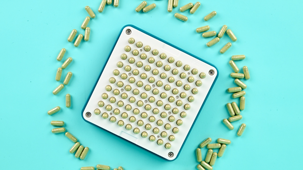 Blated 100-hole capsule filling machine tray loaded with size 00 green capsules ready to fill