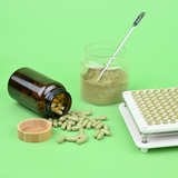 Amber glass bottle on green background with herbal capsules being poured out of it