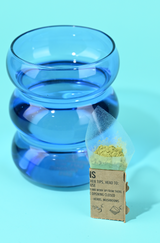 Blate Pape pouch filled with green powder with a glass of water in a blue cup behind it