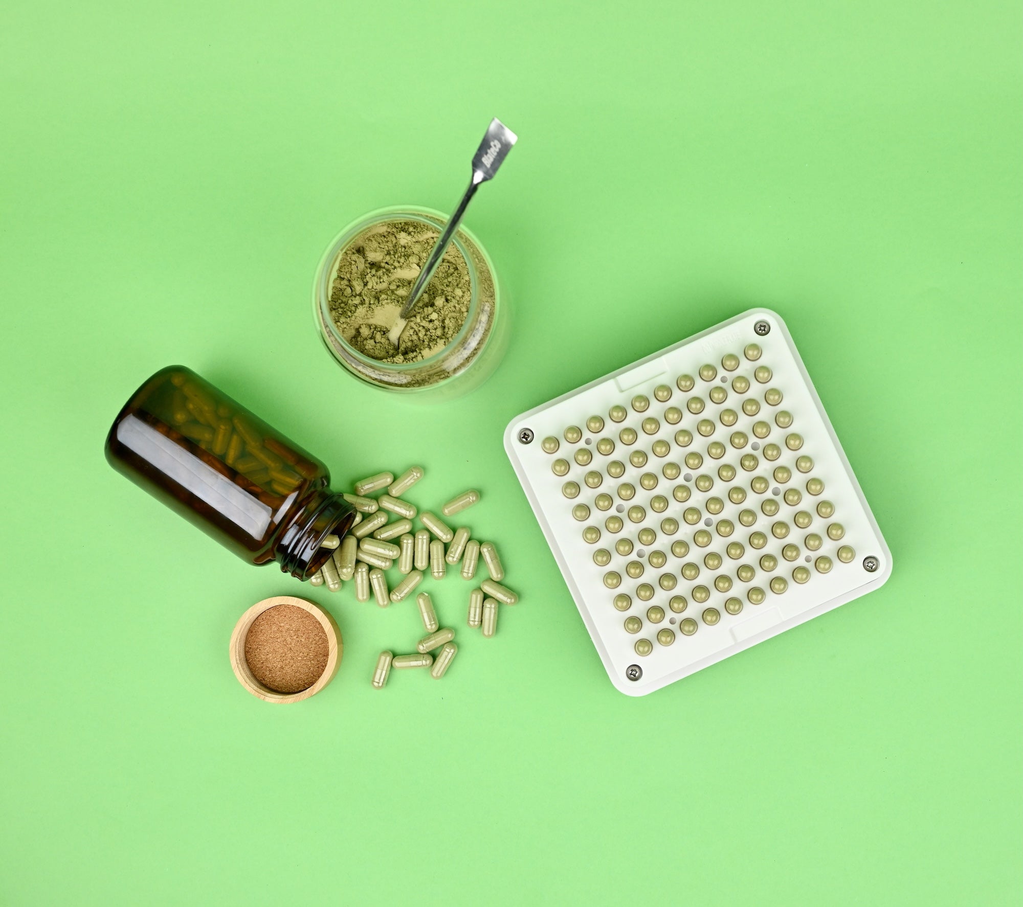Capsule filler machine with capsules, an amber glass bottle, and clear jar of green powder #color_transparent