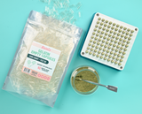 Capsule filler with green powder capsules, glass jar of green powder, and a bag of Blated Gelatin Capsules opened with capsules pouring out #color_teal